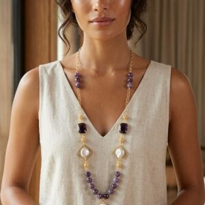 Collana artigianale lunga con pietre di ametista viola, perle barocche in rombi dorati su modella con vestito di lino chiaro.